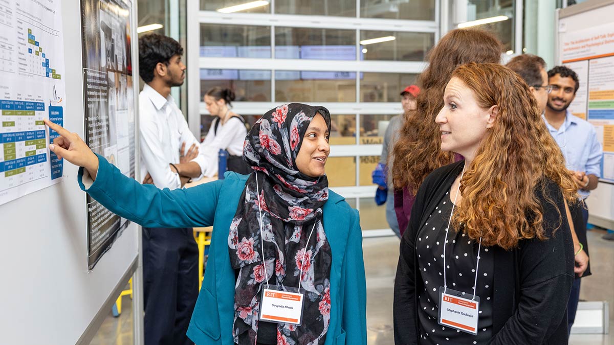 A student gives a poster presentation to a visitor at a research symposium.