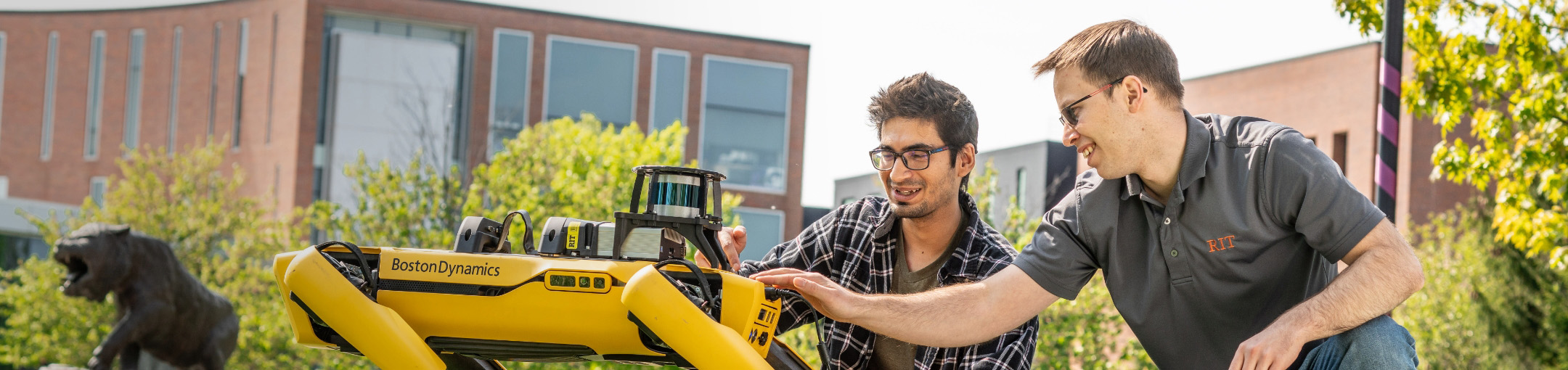 two people are interacting with a Boston Dynamics robot outdoors on campus.
