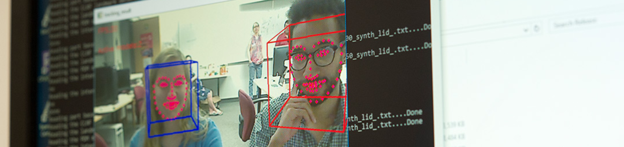 a computer screen that hasa video of two people who are sitting in front of the monitor being tracked and has squares around their heads and dots plotting their faces.