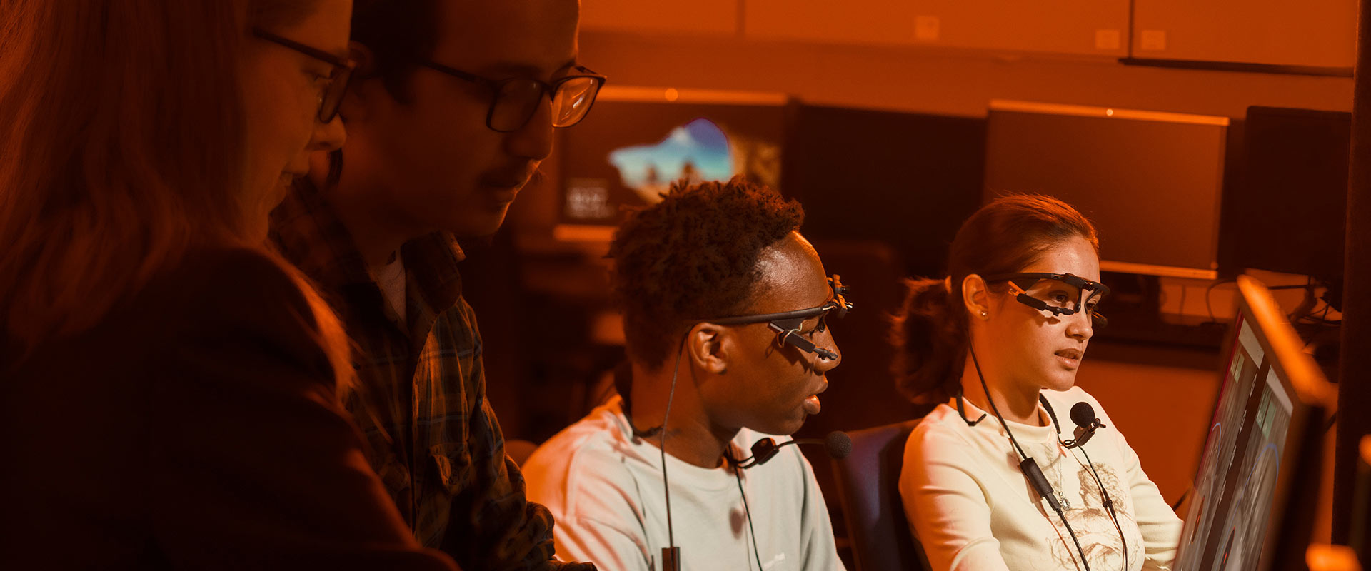 two students wearing eye tracking glasses look at a computer screen.