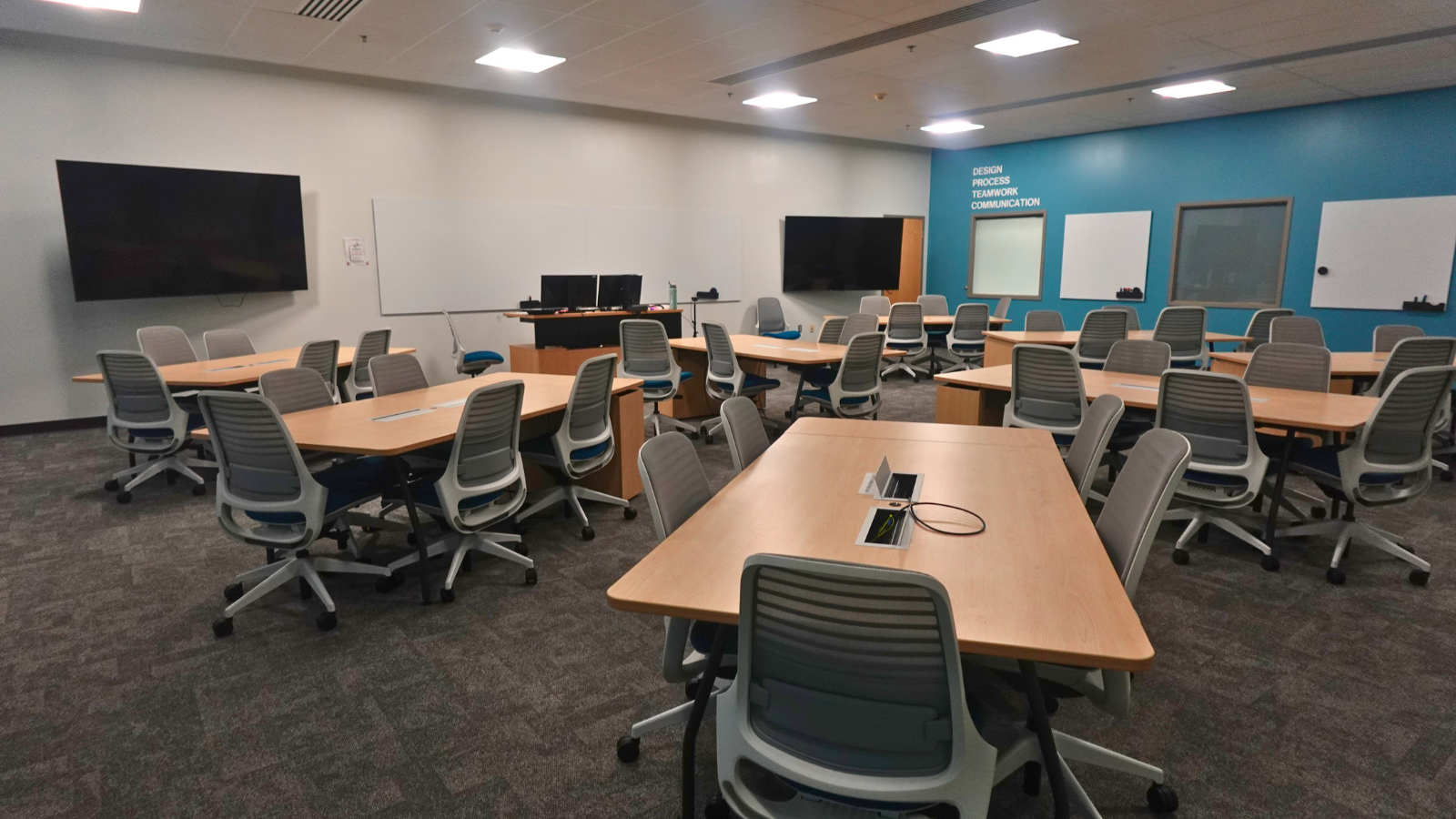 Large modern classroom with tables, monitors, and chalkboards