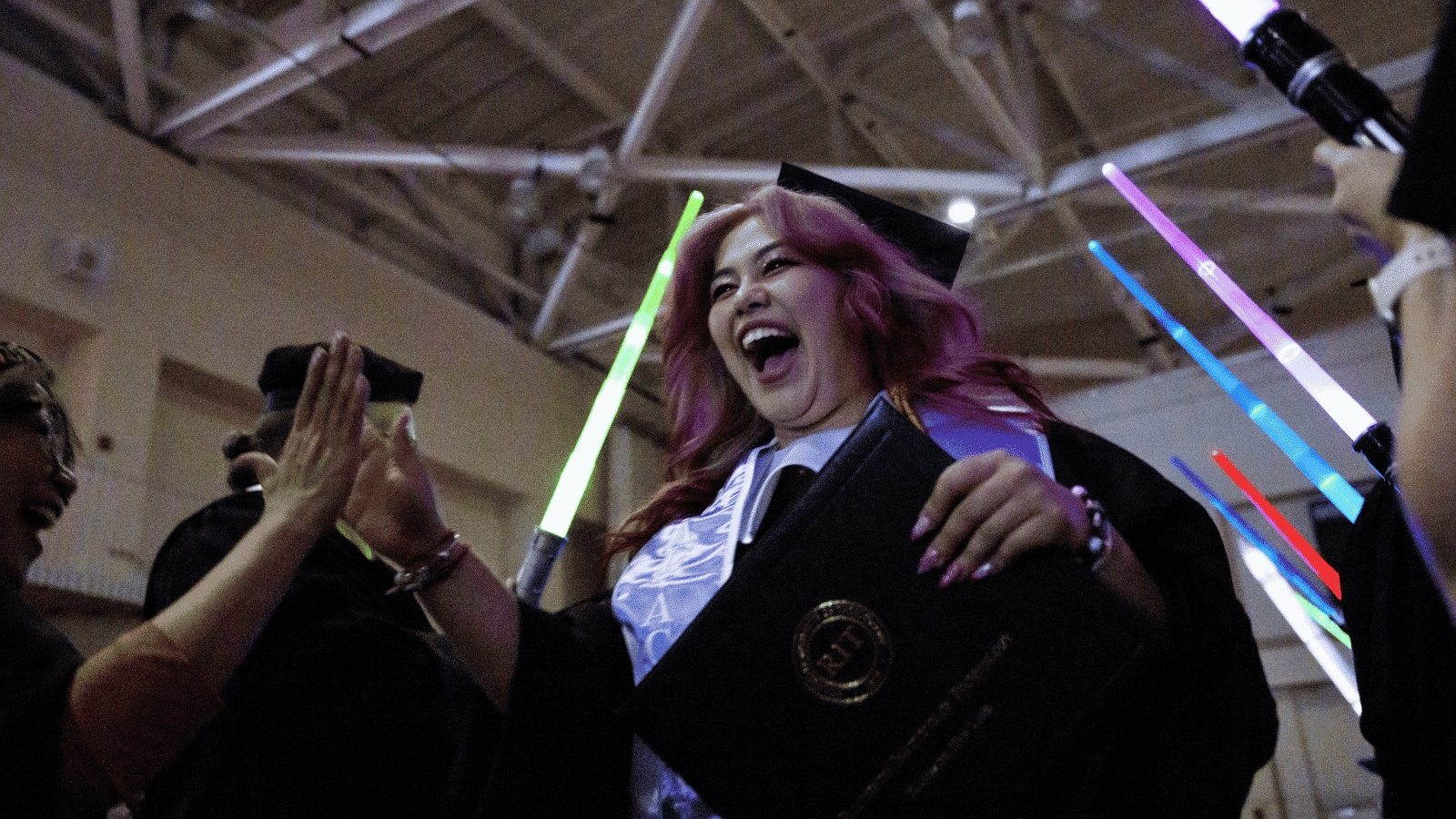 IGM graduate Ariel Cthwe walking through lightsaber tunnel after crossing the stage on Saturday, May 9, 2026