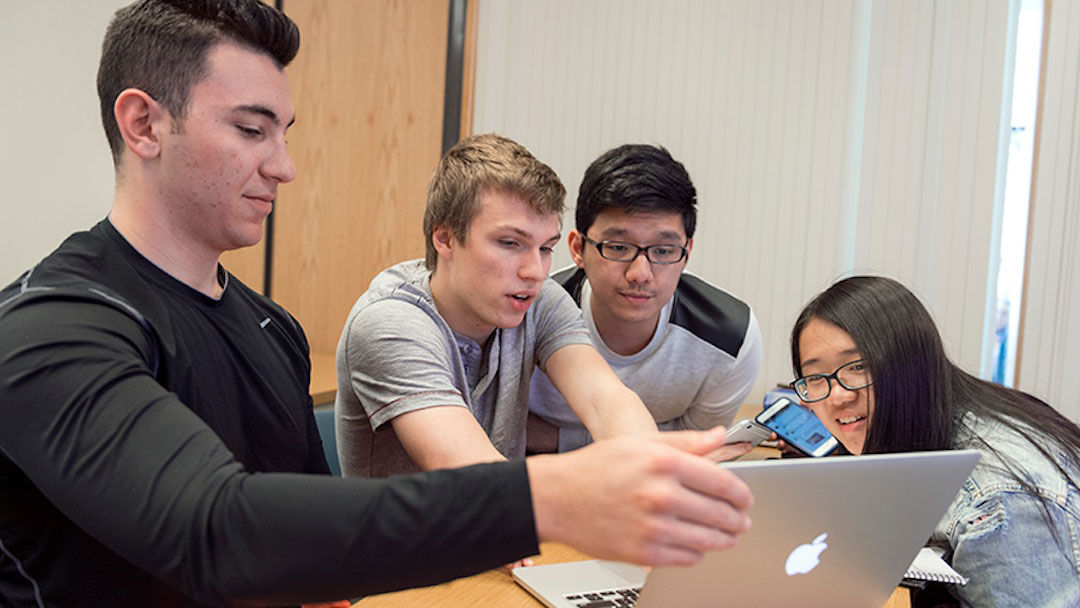 A group of students working together on a laptop and smartphone during a classroom activity.