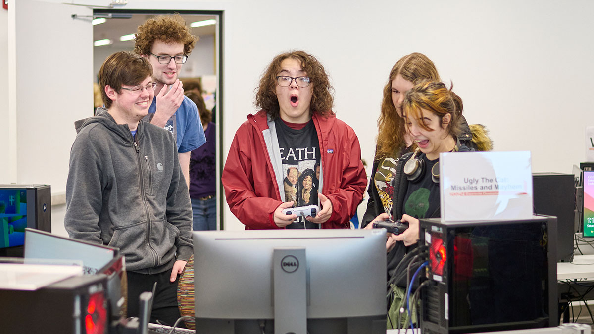 A group of students excitedly playing a video game on a large screen during a gaming event.
