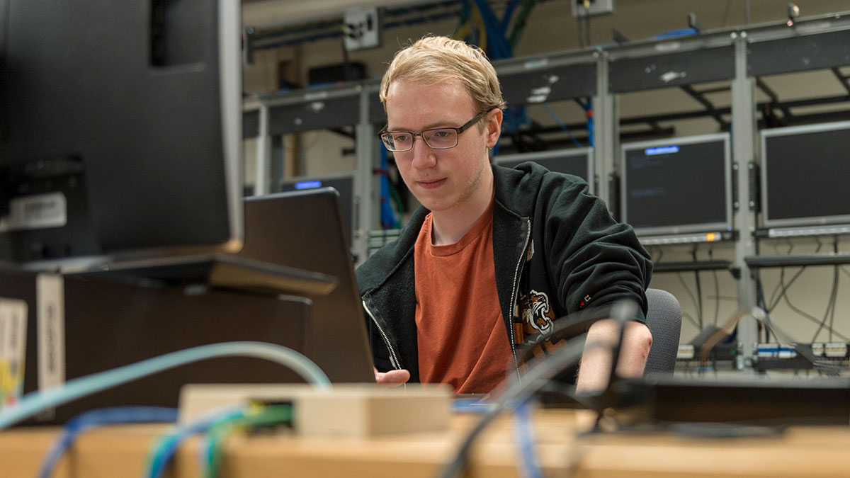 A student working with computer equipment in a network engineering lab with monitors and cables.