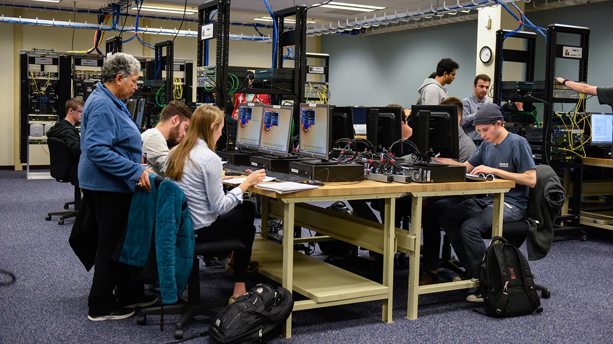 Students working collaboratively in a classroom with colorful wires and equipment in the background.