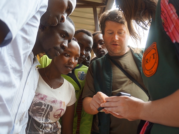 Brian Tomaszewski surrounded by team at Rwandan refugee camp looking at mobile phone