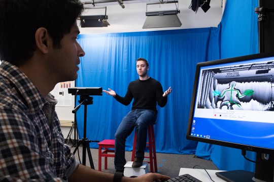 a person using A S L which is being recorded and monitored by another individual on a computer with a camera and interpretive software.