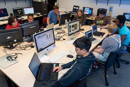 Students sitting around a desk, using computers.