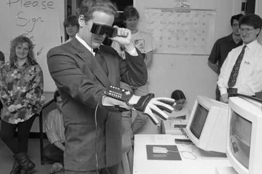 black and white photo of person using goggles and a glove with a computer controller on it.