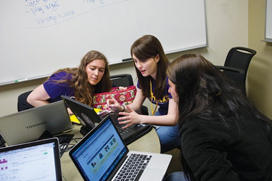 three students collaborate while looking at laptop screen.