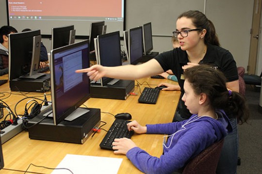 RIT student pointing to computer screen teaching grade school student.