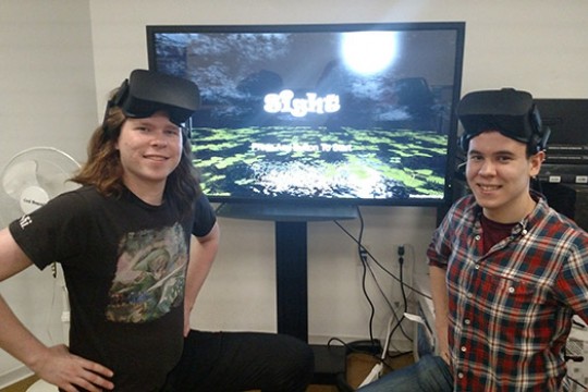Two students wearing VR headsets next to screen