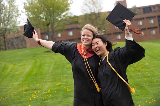 two graduating students wearing cap and gown smiling for photo.