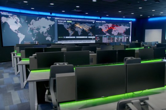 large room with three projector screens in front and several computer stations.