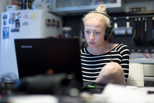 woman wearing a headset and looking at a computer while sitting in a kitchen.
