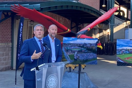 two people standing at a podium at the entrance of a baseball stadium.
