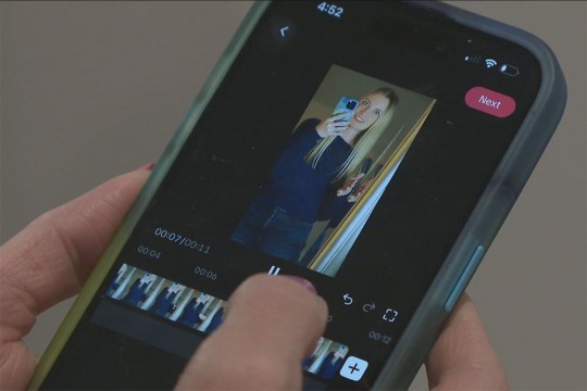 a hand holds a phone with a video being edited displayed.