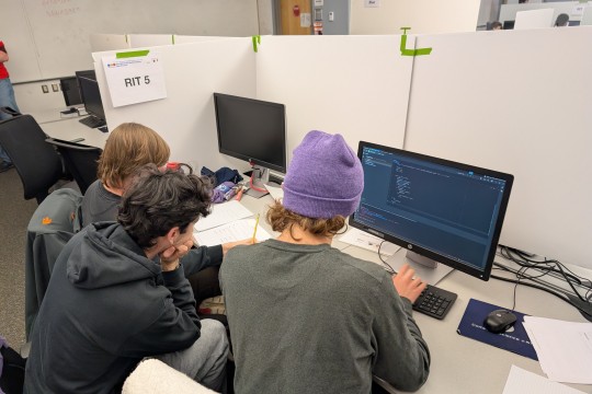 Three RIT students working around a computer