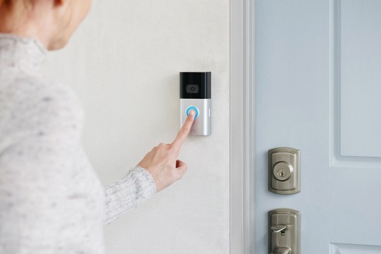 a woman presses the button on a Ring doorbell.