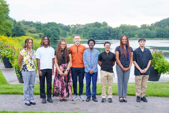 a group of college age students stand in a park like setting.