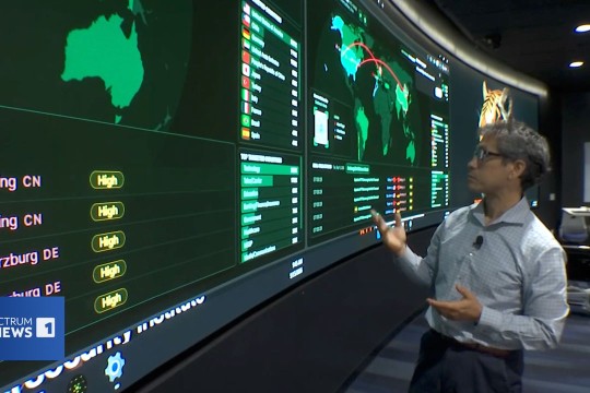 a man stands next to a large screen of cyber security data