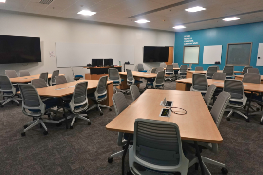 Large modern classroom with tables, monitors, and chalkboards