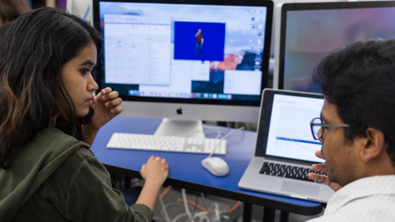 Two students talking while working on a computer
