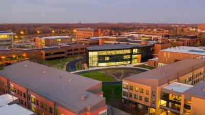 drone shot of the ESL Global Cybersecurity Institute, a black building with lit up windows surrounded by brick buildings on RIT campus.