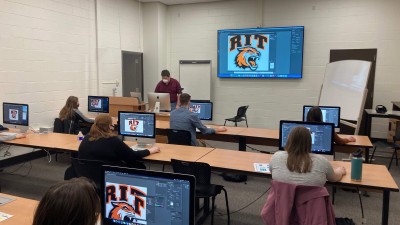 students in a computer lab follow along with their professor editing the R I T athletics logo.