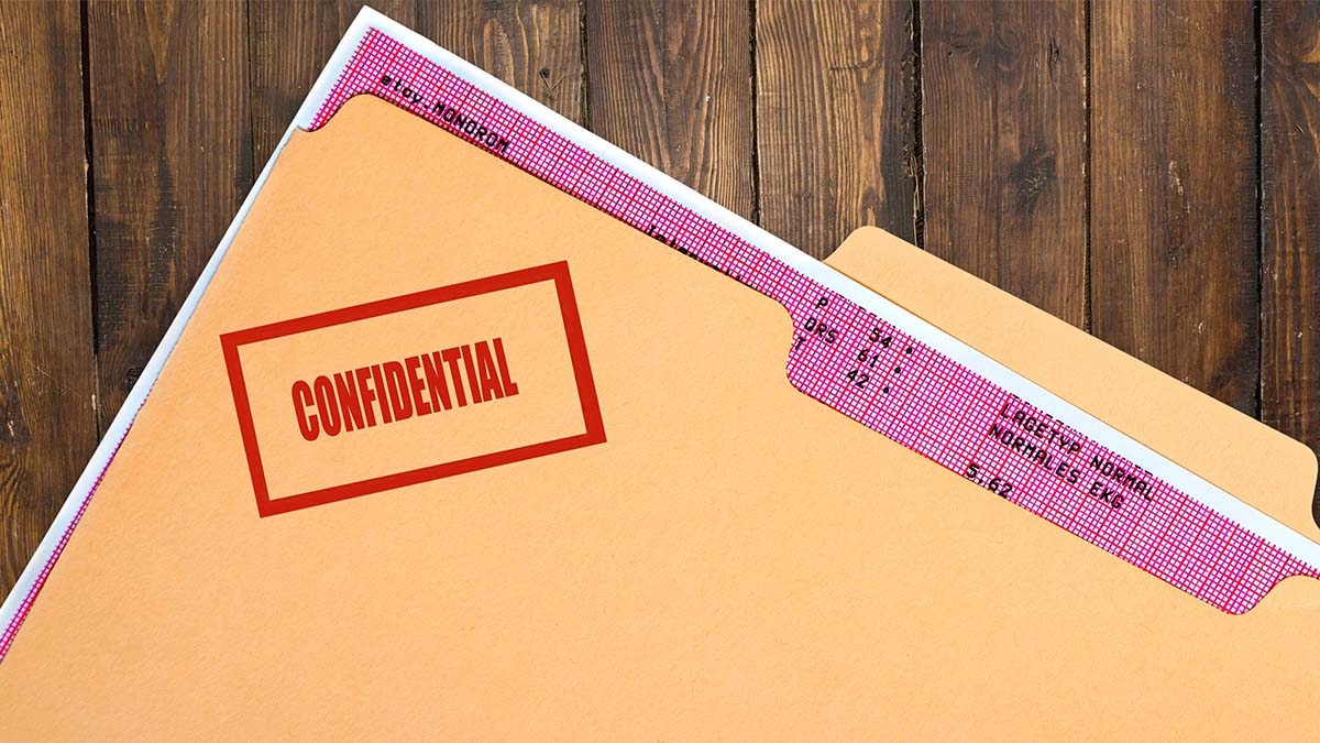 Folder labeled “CONFIDENTIAL” in red text, partially open on a wooden surface with a red-patterned tab showing printed text.