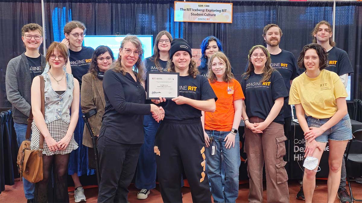 group of college students posing at Imagine R I T, with the student in the center holding a certificate.
