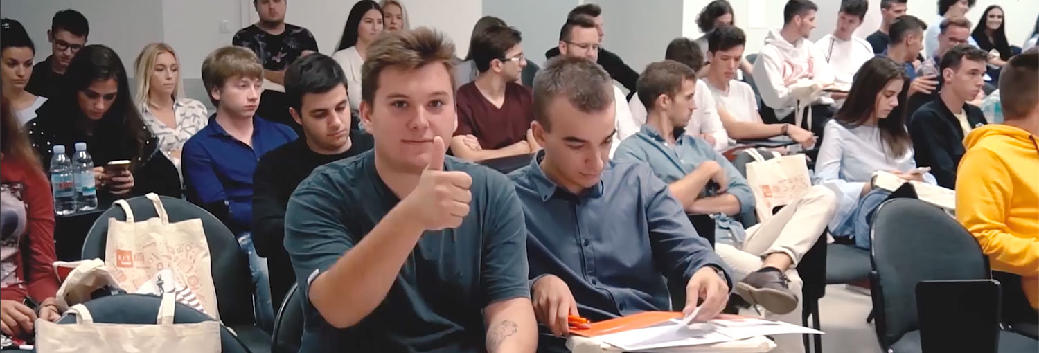 Student giving a thumbs up to the camera in a large class setting