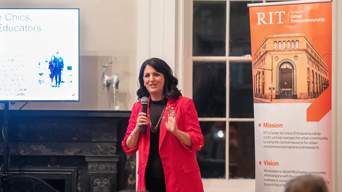 a woman holding a microphone address a crowd in a room.