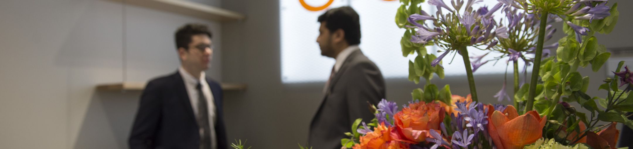 Two blury individuals standing and talking with an in-focus flower bouquet in the foreground 