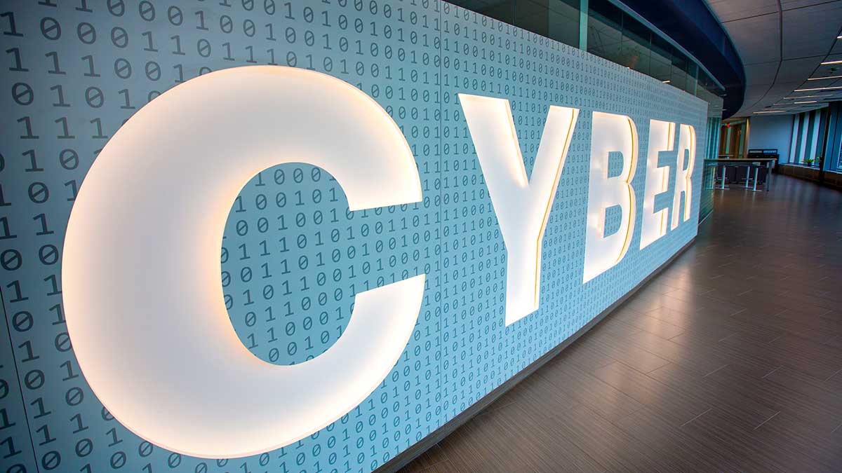 An illuminated sign with the word 'CYBER' on a wall covered in binary code patterns inside a modern cybersecurity facility.