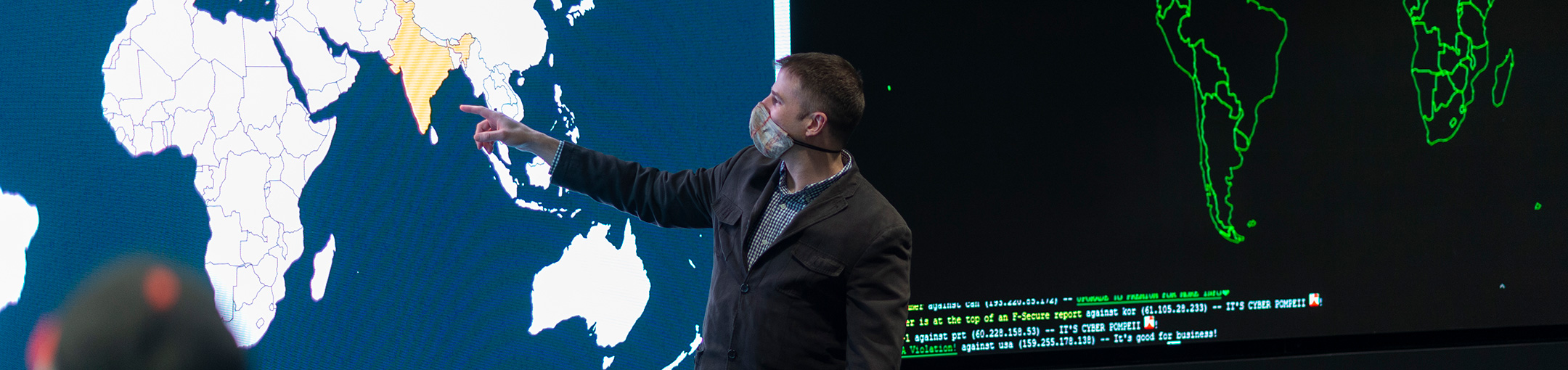 Professor pointing at a large screen displaying the globe.