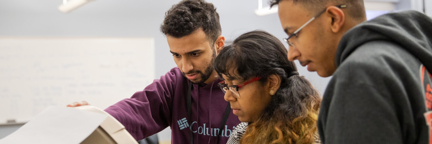 3 students looking down at a computer screen.