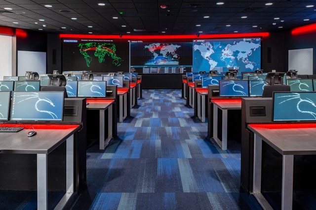 a classroom filled with computers and a backdrop of information displayed on electronic boards at the front of the room.