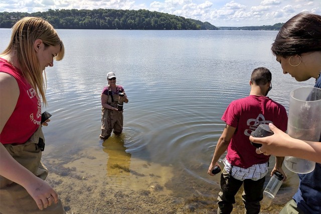 four researchers collecting sediment samples from a lake.