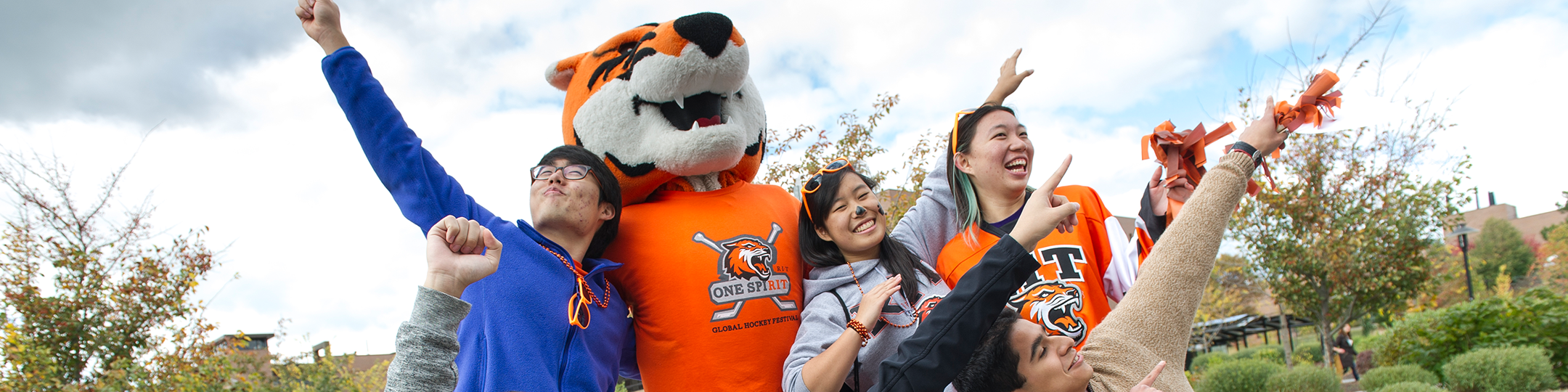 three students pose with Ritchie, dressed in RIT merchandise