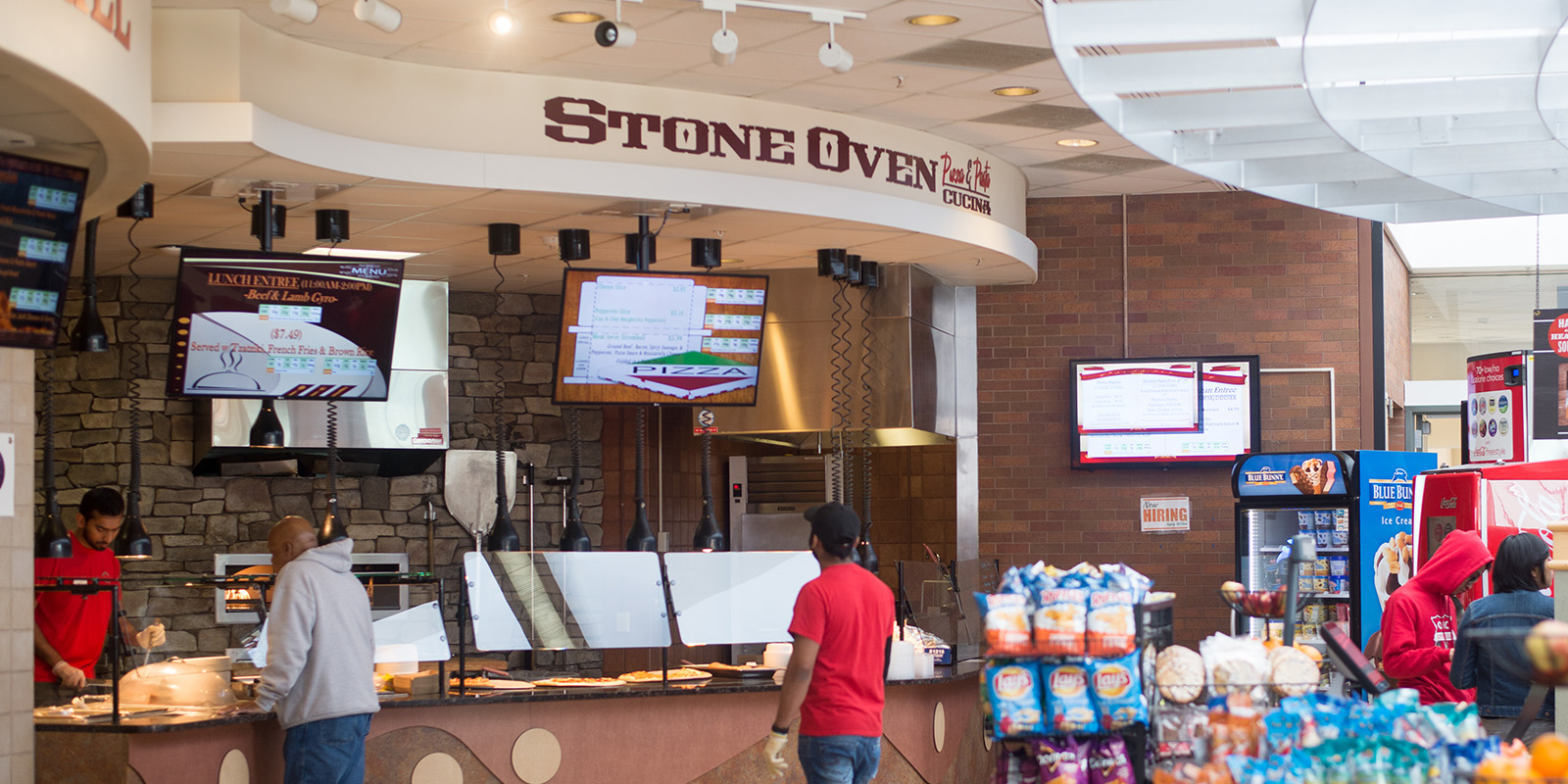 Interior of The Commons dining location with staff, digital menus, and a stone wall design.