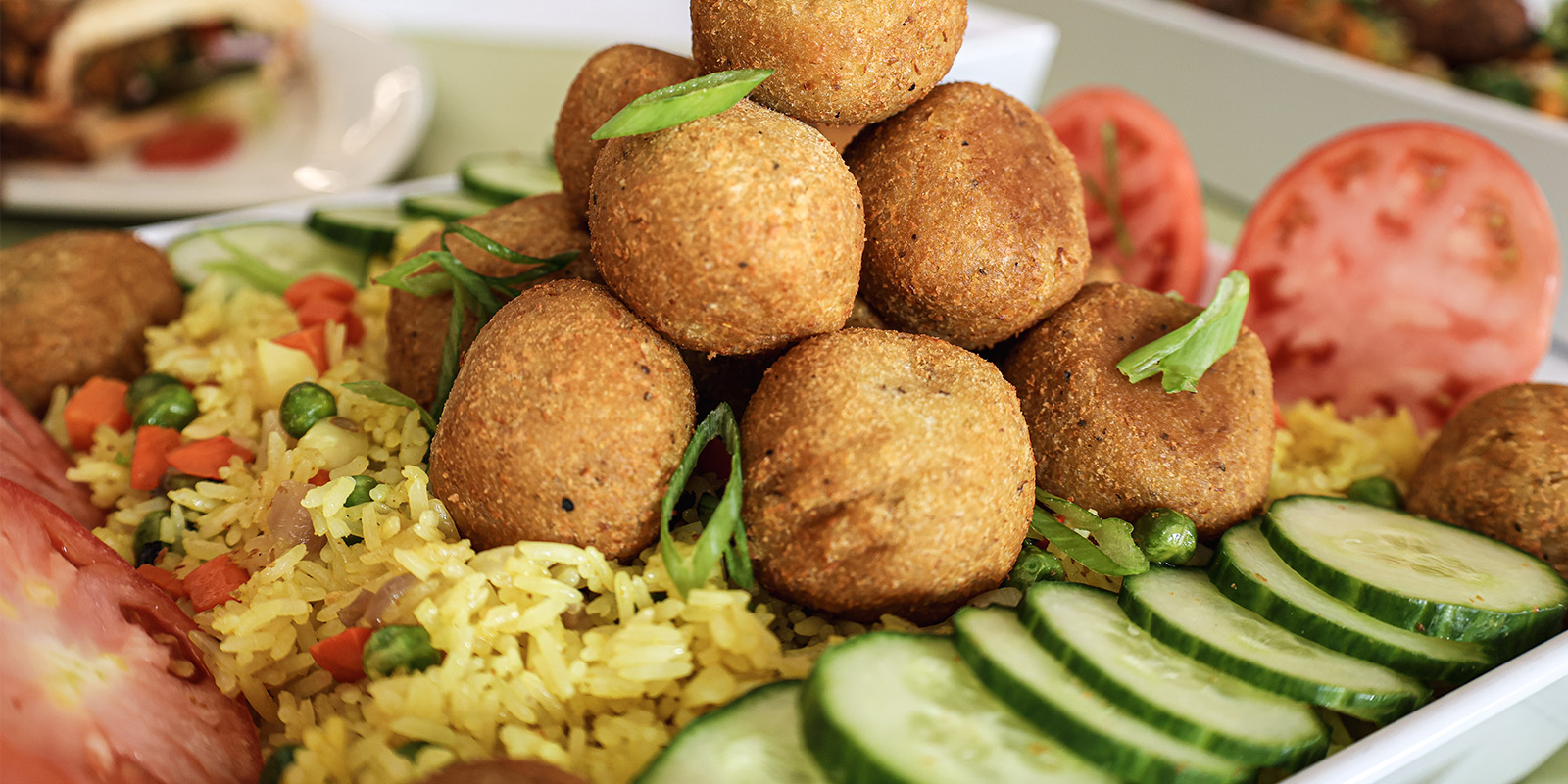 A plate of fried rice, cucumber, tomato and lentil balls