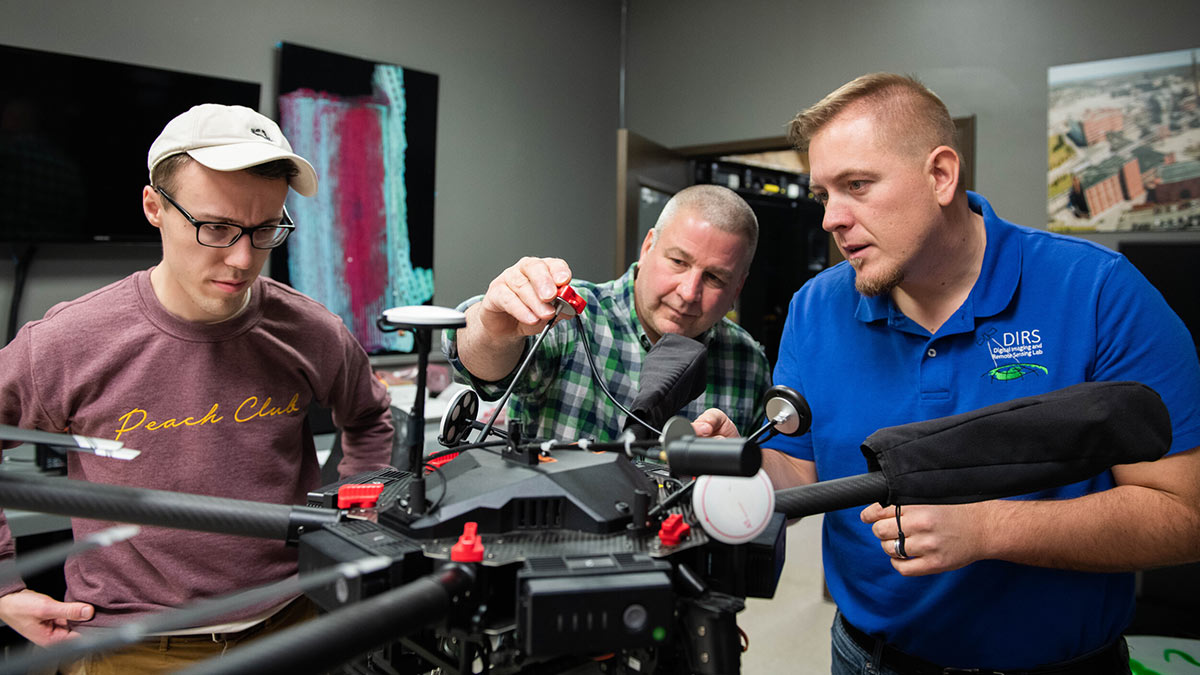 three researchers work on a drone in a lab.