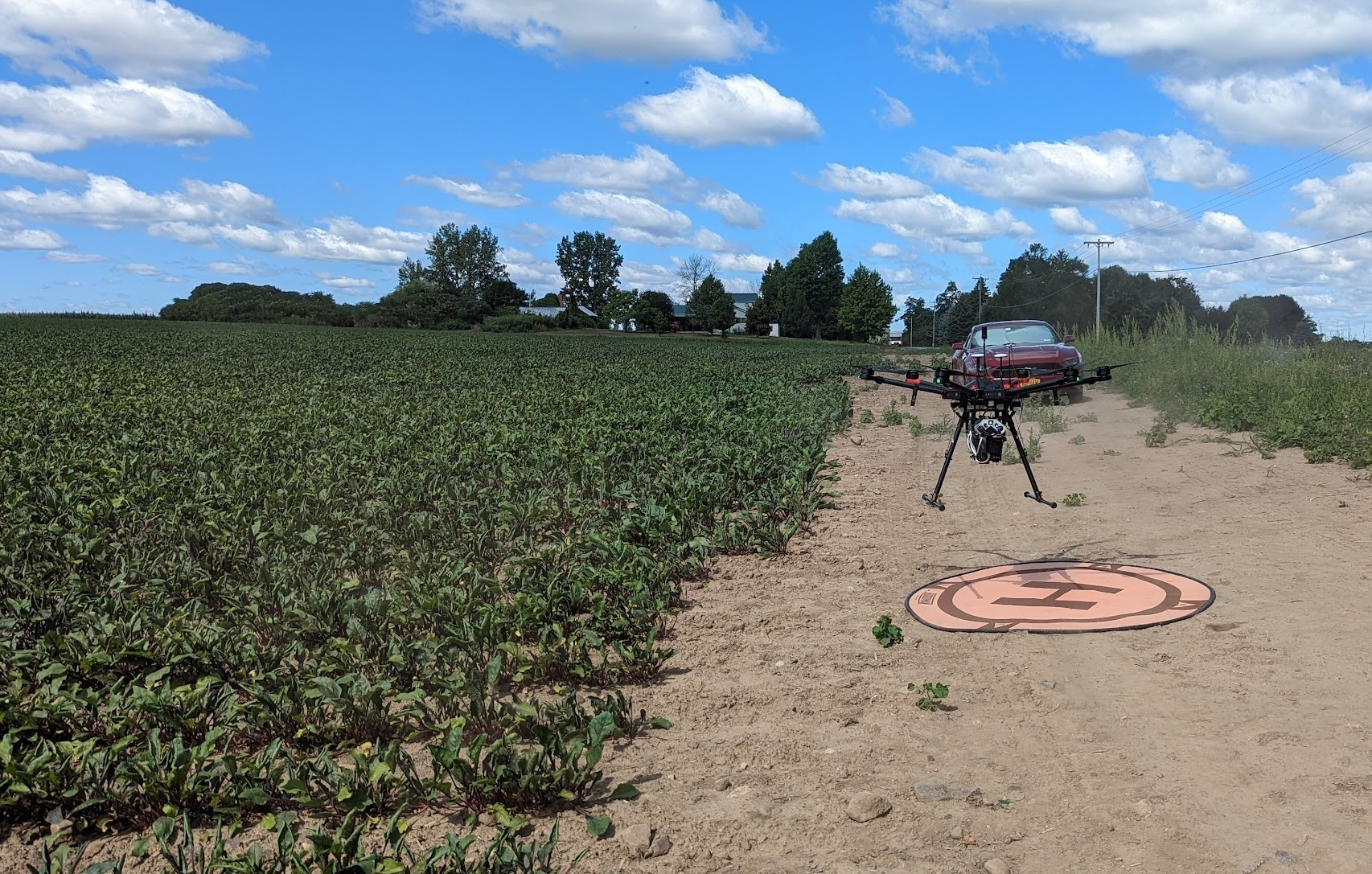 A DJI Matrice 600 (MX1) drone equipped with multimodal sensors lifting  off from a designated launch pad adjacent to a table beet field. The  flight was part of a data collection campaign aimed at monitoring crop  health and estimating yield using multispectral, hyperspectral, and  LiDAR imaging.