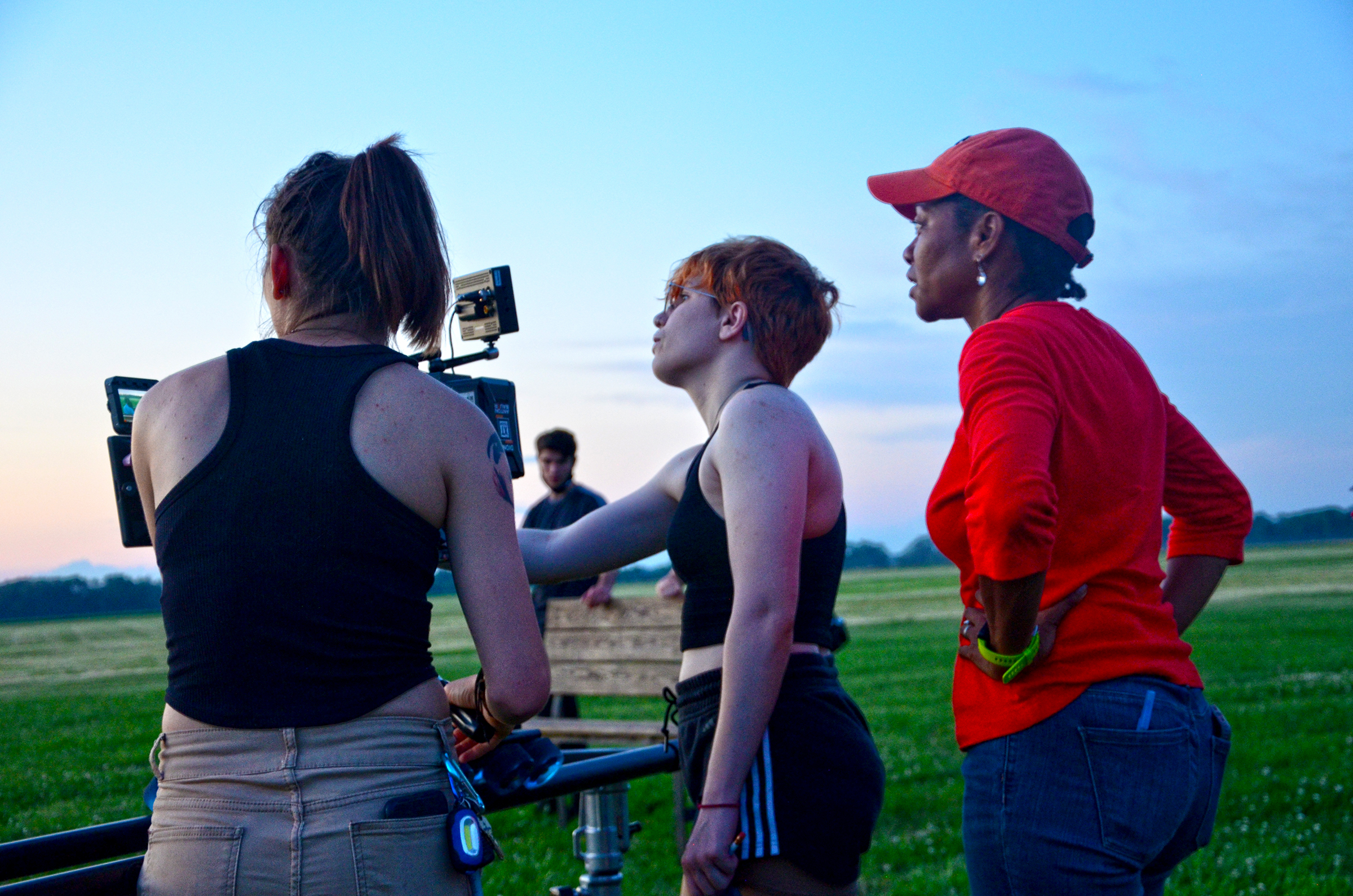 three people standing around camera in field