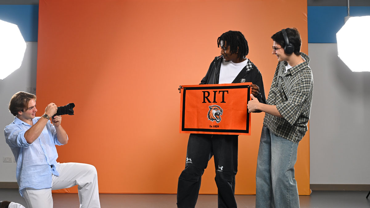Two students posing for a picture with RIT flag in hand