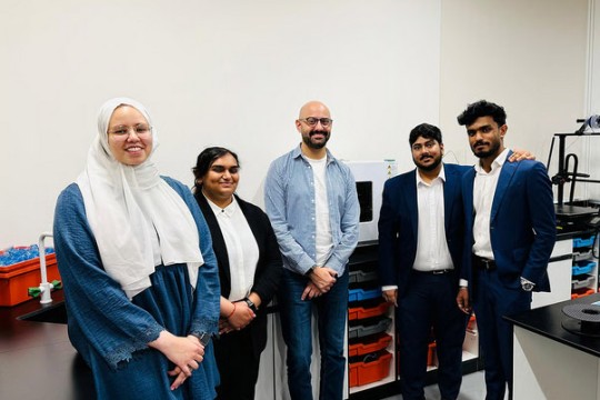 a group of people stand in a 3 D printing lab.