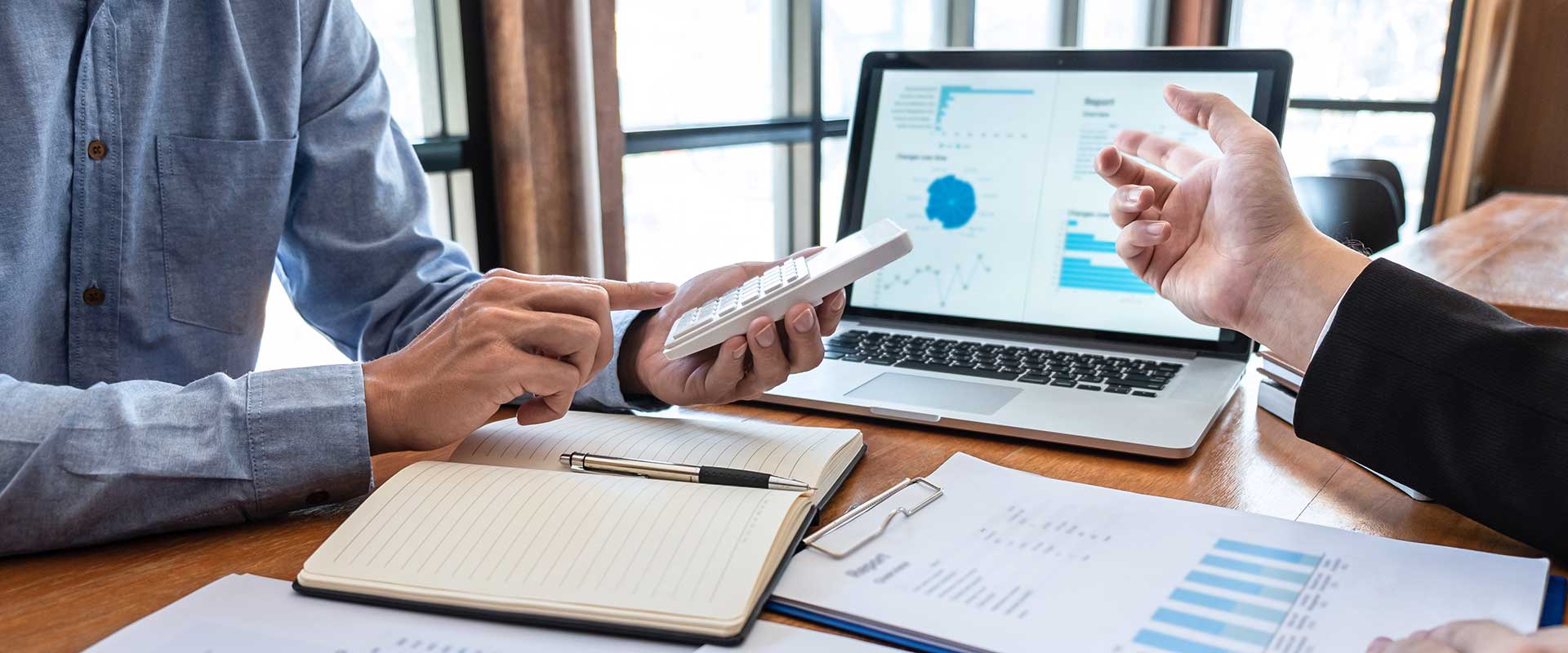 two people reviewing charts and data on a computer screen and on printouts. 