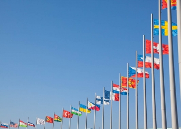 a number of international flags hanging from flag poles with a blue sky background